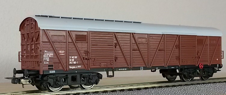 Ein einzelner, langer Eisenbahn-Güterwagen, braun mit silbernem Dach. Der Aufbau ist überwiegend aus Holz.